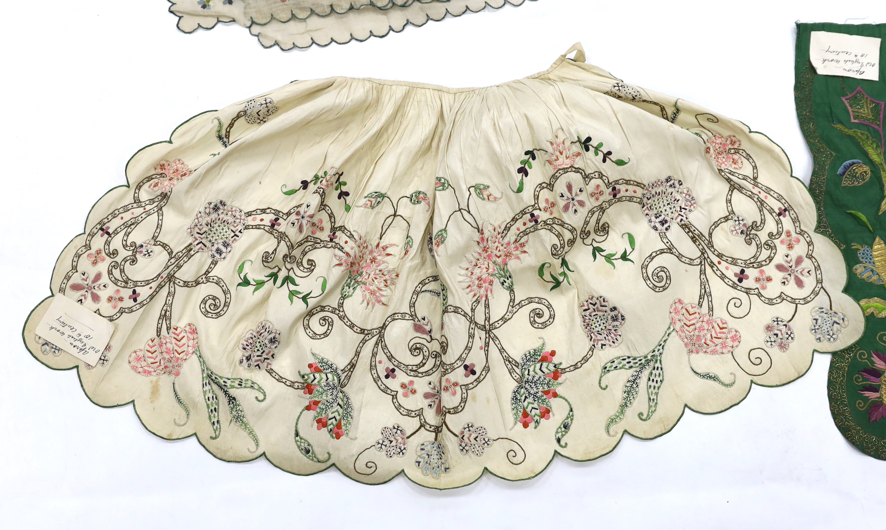 A late 18th century green silk scalloped bordered lady’s apron border, ornately embroidered with gold metallic threads and polychrome silk, in a large vine, floral and leaf design, together with a similar cream silk embr